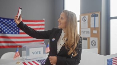 Neşeli genç sarışın bir kadın, bir Amerikan üniversitesi seçim merkezinde selfie çekiyor..