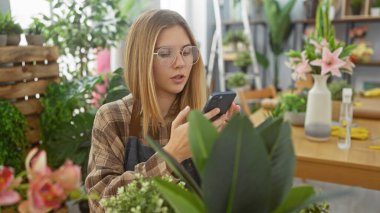 Genç bir kadın akıllı telefon kullanıyor. Etrafı çiçekçiyle çevrili.