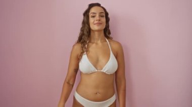 Beş numaralı parmaklarıyla işaret eden bikinili genç İspanyol kadın, izole edilmiş pembe arka planda mutlu bir şekilde gülümsüyor.