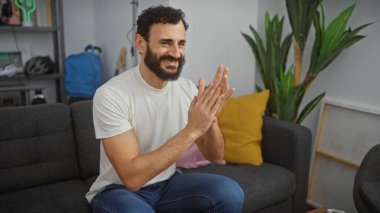 Gülümseyen sakallı adam modern oturma odasında el çırpıyor.