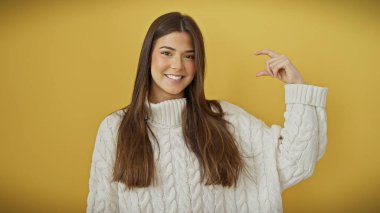 Gülümseyen genç İspanyol kadın sarı arka planda küçük bir jest yapıyor.