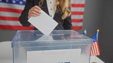 Genç bir kadın biz bayraklarla çevrili bir Amerikan seçim merkezinde oy kullanıyor..