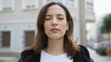 Kentsel sokak ortamında gözleri kapalı, dingin, genç İspanyol bir kadın, güzellik ve huzur sergiliyor..