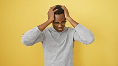 Gözlüklü, sarı arka planda kafasını tutan stresli genç adam.