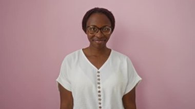 Genç Afro-Amerikalı kadın, neşeli, olumlu bir gülümsemeyle, pembe bir arka plan üzerine gözlük takarak seni işaret ediyor.
