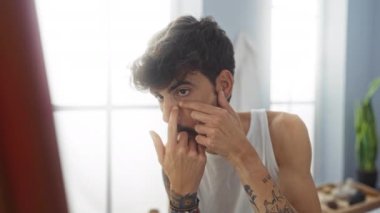 Yüzünde sivilce olan sakallı genç bir adam. Kapalı bir güzellik salonunda dövmeli kolları ve ciddi bir ifadeyle.