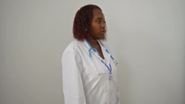 Doktor, üniformalı, kendine güvenen ve izole edilmiş beyaz bir arka plan üzerinde ciddi bir şekilde düşünen, kendine güvenen, ciddi bir tavır takınan Afro-Amerikan kadını.