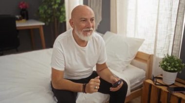 Evde rahat bir yatak odasında televizyon seyrederken sakallı, neşeli bir adam. Yatak, bitki ve masa ile iç mekan ayarlarıyla karakterize ediliyor..