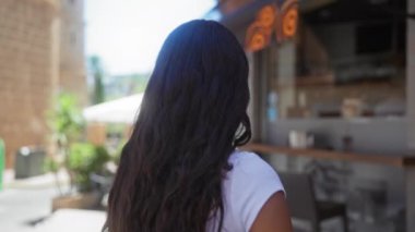 İspanyol bir kadın şehir caddesinde yürüyordu, yukarı bakıyordu ve uzun esmer saçlarıyla gülümsüyordu ve beyaz gömlek giyiyordu.
