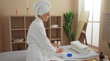 Kaplıca merkezindeki beyaz bir kadın, beyaz bir bornoz ve havlu giyerken ellerine losyon sürüyor..