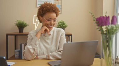 İyi dekore edilmiş bir oturma odasında dizüstü bilgisayar kullanan gülümseyen kadın üretkenlik ve konfor taşıyor..