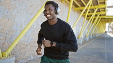 Açık hava ortamında kulaklıkla koşan gülümseyen Afrikalı bir adam sağlığını ve aktif yaşam tarzını gösteriyor..