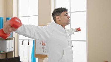 Parlak fizyoterapi kliniğinde dambıllarla egzersiz yapan yakışıklı bir adam.