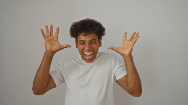 Latin kökenli genç adam, beyaz arka planda izole edilmiş elleri havada sevinç ifade ediyor.