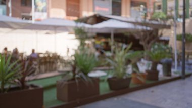 Bitkilerin ve arka planda insanların olduğu bulanık açık hava kafe sahnesi, bokeh etkisi ve kentsel yerleşim alanının dağıtılması.