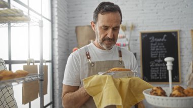 İspanyol adam fırında yeni pişmiş bir turtayı arka planda çeşitli hamur işleriyle tutuyordu. Önlük giyiyordu ve evde dikiliyordu..