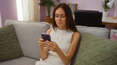 Genç kadın rahat oturma odasında akıllı telefon kullanıyor, esmer, çekici, yetişkin, dinlendirici, ev, ev, ev, ev, daire, kadın.