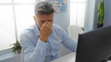 Handsome caucasian man looking stressed in an office workspace with a computer and indoor plants