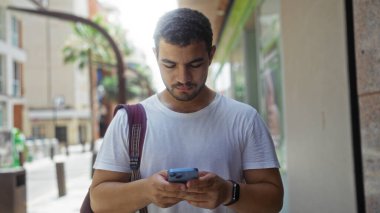 Şehir caddesinde akıllı telefon kullanan yakışıklı genç adam.