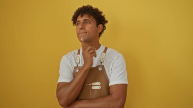 Yakışıklı genç İspanyol adam izole edilmiş sarı bir arka plana karşı düşünüyor..