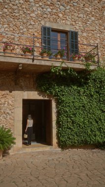 Bir kadın Mallorca İspanya 'da sarmaşıklı taştan bir eve giriyor güneşli mavi gökyüzünün altında