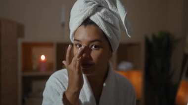 Genç, çekici bir kadın huzurlu bir spa odasına cilt bakımı uyguluyor. Ilık ışıklandırması ve rahatlatıcı bir ambiyansı var..