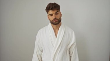 Bornoz giymiş genç İspanyol bir adam. Kafası karışık ve cahil bir ifade takınıyor. İzole edilmiş beyaz bir arka plan üzerinde şüpheyle duruyor.