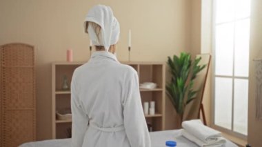 Havlu ve bornoz giyen çekici bir kadın spa sağlık odasında el hareketi yapıyor.