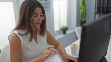 Genç bir kadın gözlüğünü çıkarıyor ve iş yerinde yorulmadan esniyor.