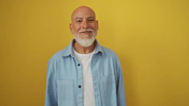 Üst düzey bir adam, kel ve kot gömlek giyiyor, izole edilmiş sarı arka planda dikiliyor, kulağından girip kulağından çıkan dedikoduları dinliyor, sağırlık söylentileriyle yüzleşiyor.