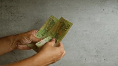 Arjantinli pezoları sayan adam, arka planda kağıt parayla el ele tutuşuyor.