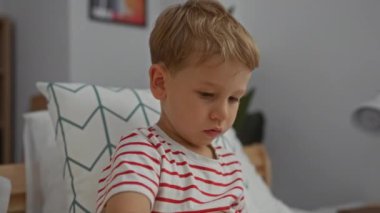 Küçük çocuk, sarı saçlı. Yatak odasında oyuncaklarla oynuyor.