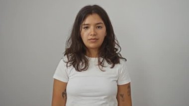 Yüzünde şüpheli bir ifade olan beyaz tişört giyen genç İspanyol kadın, ağzı açık ve dışlanmış bir arka planda alaycı bir ifade var.