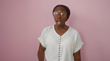 Genç Afro-Amerikan kadın gözlük takıyor, ağzı açık şüpheci duruyor ve pembe arka planda alaycı bakışlar atıyor.