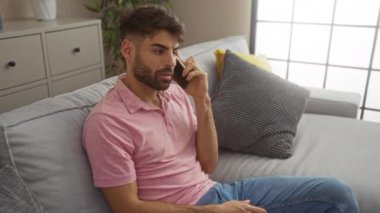 Genç adam modern bir oturma odasında telefonla konuşurken kapalı bir yumrukla kutluyor.