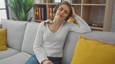 Rahat genç bir kadın, şık dekorlu rahat bir oturma odasında kulaklıklarla müzik dinlemekten hoşlanır.