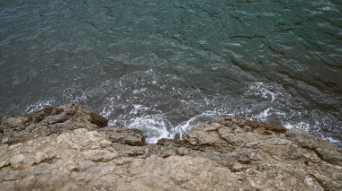 Okyanus dalgaları gündüz vakti kayalık kayalık kıyılara çarpıyor, sakin ve doğal bir kıyı manzarası sergiliyor..