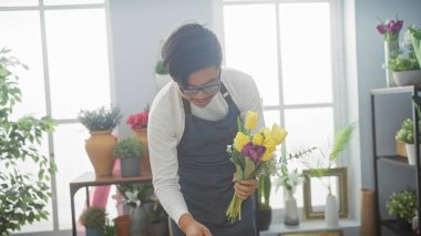 Parlak bir çiçekçide renkli çiçekler düzenleyen Asyalı genç bir adam..