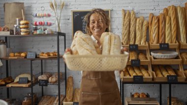 Fırında ekmek tutan kadın arka planda raflarda çeşitli fırınlanmış ürünler sergiliyor.