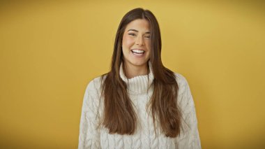 Beyaz kazaklı gülümseyen İspanyol kadın sarı arka planda poz veriyor..