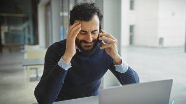 Telefonda dizüstü bilgisayarlı stresli bir adam, hayal kırıklığını ve baş ağrısının eşlik ettiği rahatsızlığı dile getiriyor.