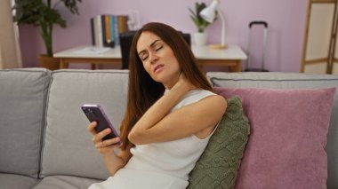 Oturma odasındaki kanepede telefonu olan bir kadın boynu ağrıyor.