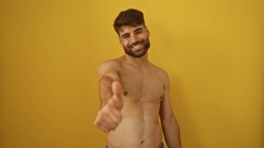 Sakallı, gülümseyen ve baş parmak işareti yapan genç bir İspanyol, sarı bir arka planda izole edilmiş, mutlu ve kendinden emin bir tavır sergiliyor..