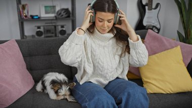 İspanyol kadın, rahat bir oturma odasındaki kanepede bisikletli teriyerinin yanında kulaklıkla müzik dinlemekten hoşlanır.