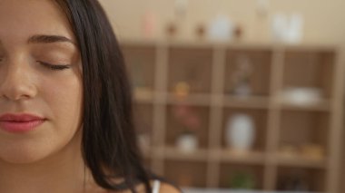 Kaplıcada gözleri kapalı bir şekilde rahatlayan genç bir kadın, yumuşak odaklı bir arka planı olan bir sağlık merkezinde sakin bir anın tadını çıkarıyor..