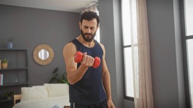 Orta yaşlı bir adam modern bir yatak odasında dambılla egzersiz yapıyor.