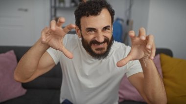 Modern bir oturma odasında sakallı, neşeli, orta yaşlı bir adam.