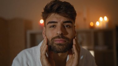 Sakallı yakışıklı genç adam, çevresindeki mum ışığı olan bir sağlık merkezinde rahatlatıcı bir anın tadını çıkarıyor.