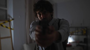 Kravatlı adam dikkat bandı ve karanlık ambiyansı olan loş bir olay yerine tabanca doğrultuyor..