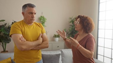 Orta yaşlı bir adam ve bir kadın, bitkiler ve doğal ışıkla dolu sıcak, kapalı bir oturma odasında ciddi bir konuşma yapıyorlar..